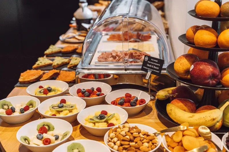 Un buffet propose des fruits frais, des viennoiseries et de la charcuterie.
