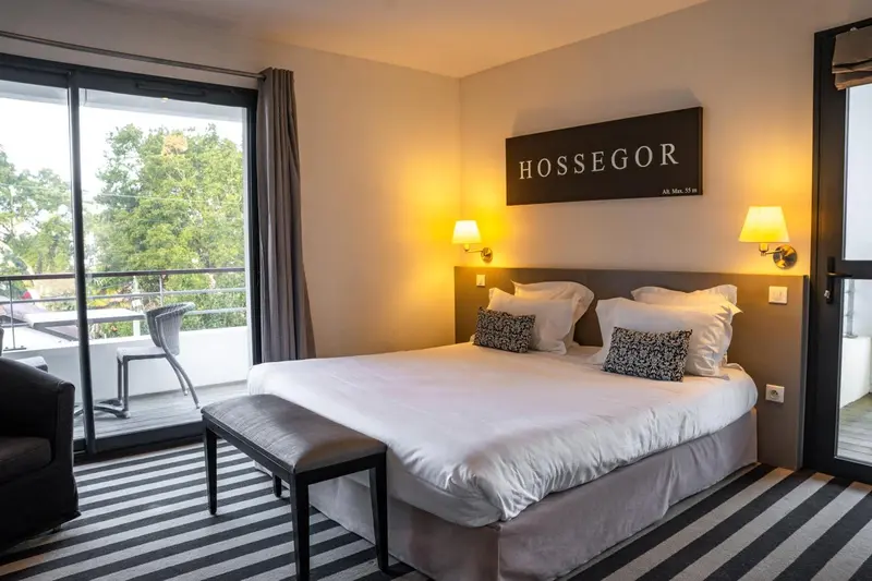 Chambre lumineuse avec un grand lit et un accès à un balcon.