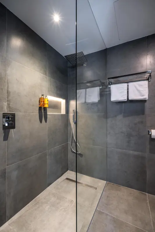 Une douche à l'italienne moderne avec des carreaux gris et des serviettes blanches.