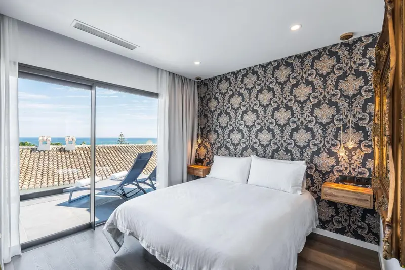 Une chambre lumineuse avec un grand lit donnant sur une terrasse et la mer.