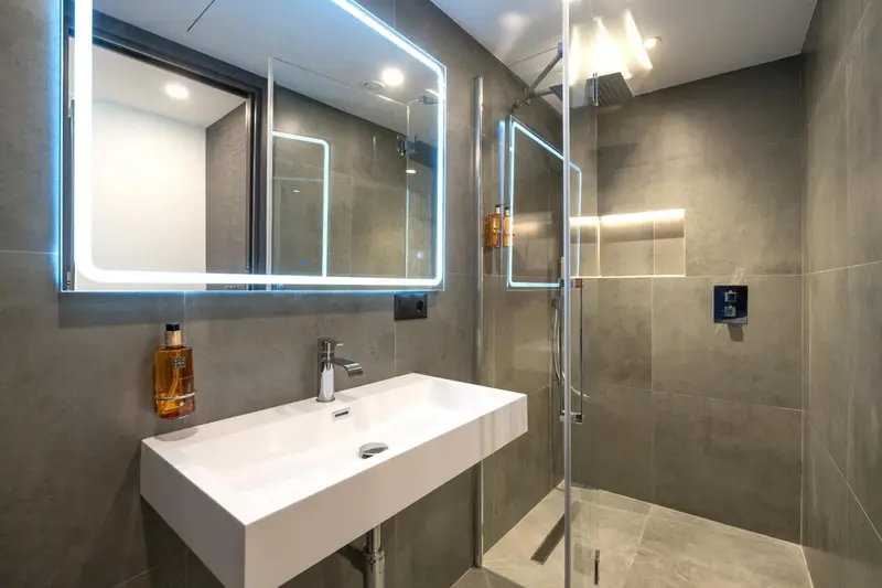 Une salle de bain moderne avec douche à l'italienne et grand miroir lumineux.
