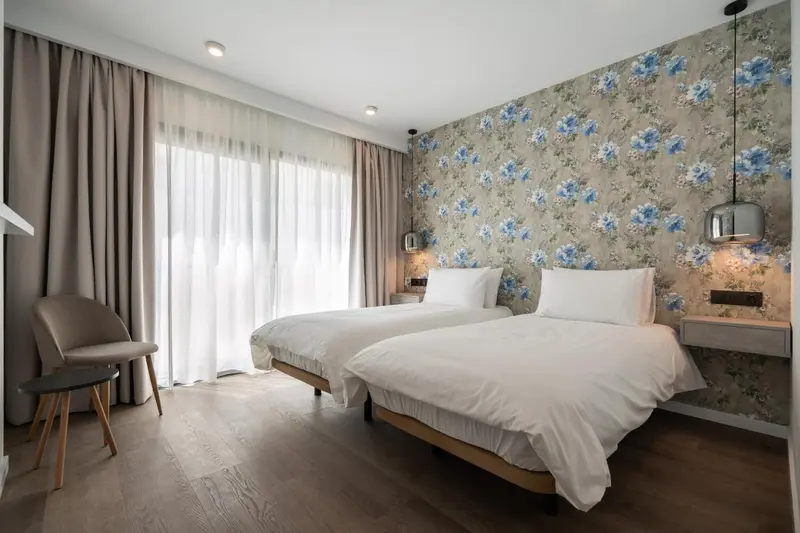 Une chambre lumineuse avec deux lits simples et un mur floral.