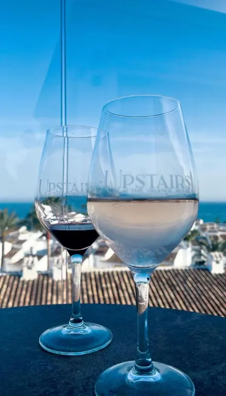 Deux verres de vin sont posés sur une table face à une vue sur la mer.