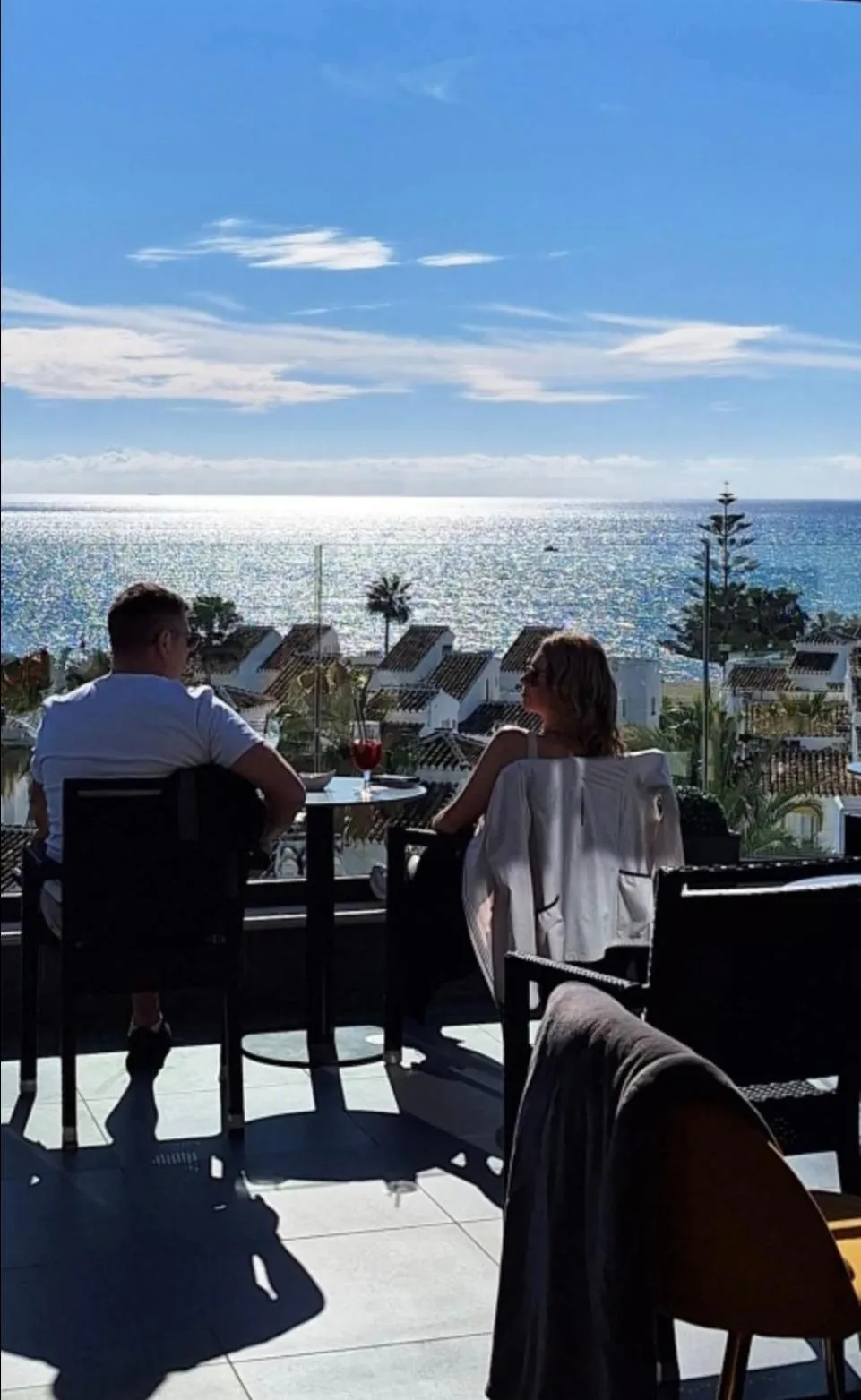 Deux personnes sont assises à une table sur une terrasse avec vue sur la mer.