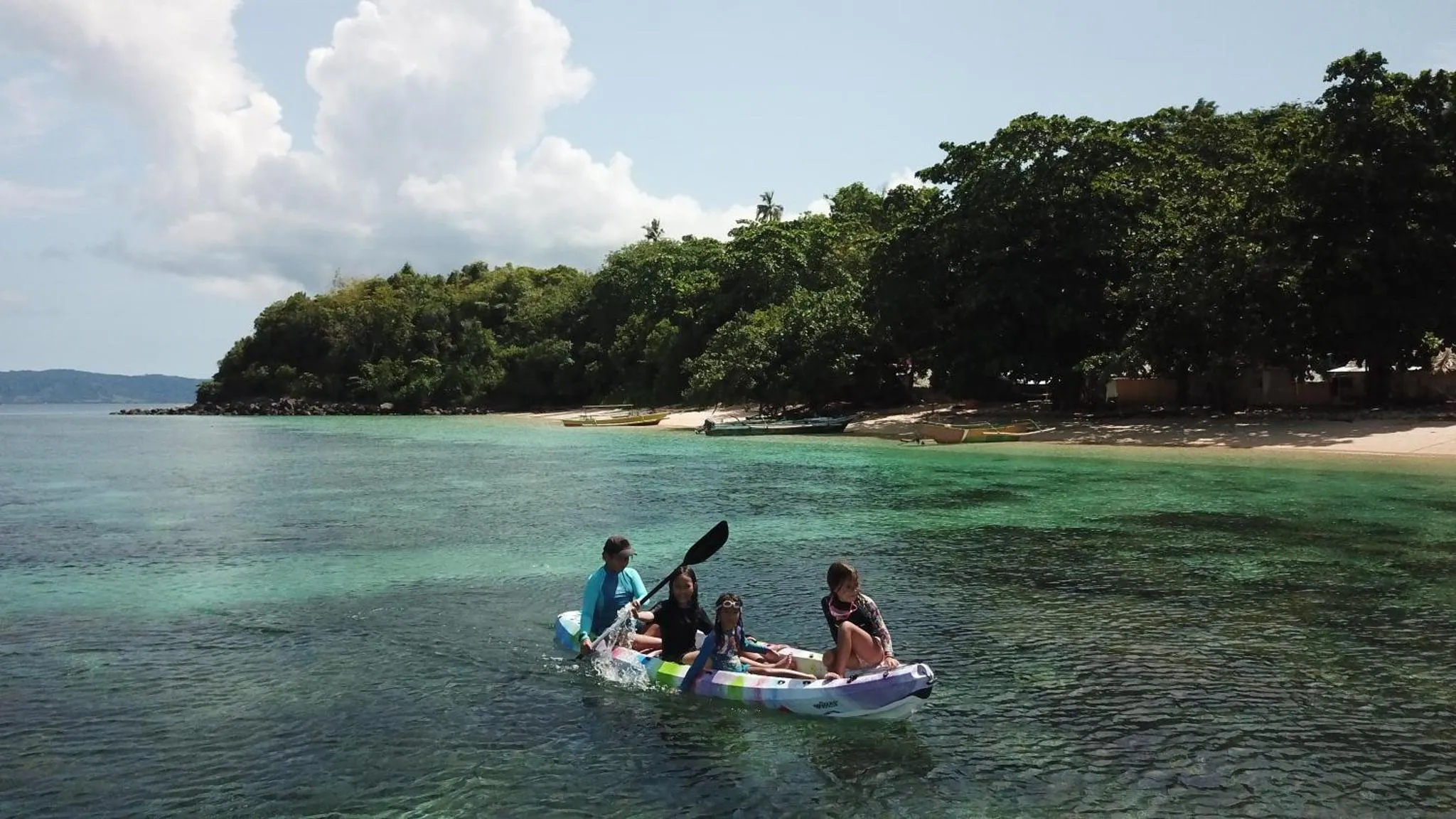 Des personnes pagayent en kayak dans une eau turquoise le long d'une côte tropicale.