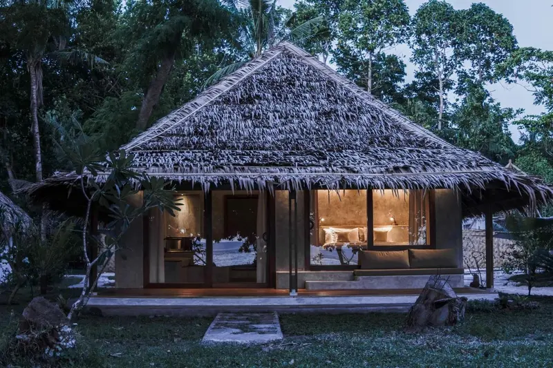 Une petite maison au toit de chaume est éclairée de l'intérieur.
