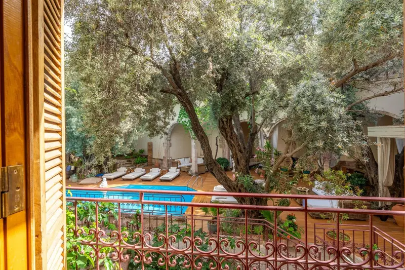 Vue d'un jardin luxuriant et d'une piscine depuis un balcon fleuri.