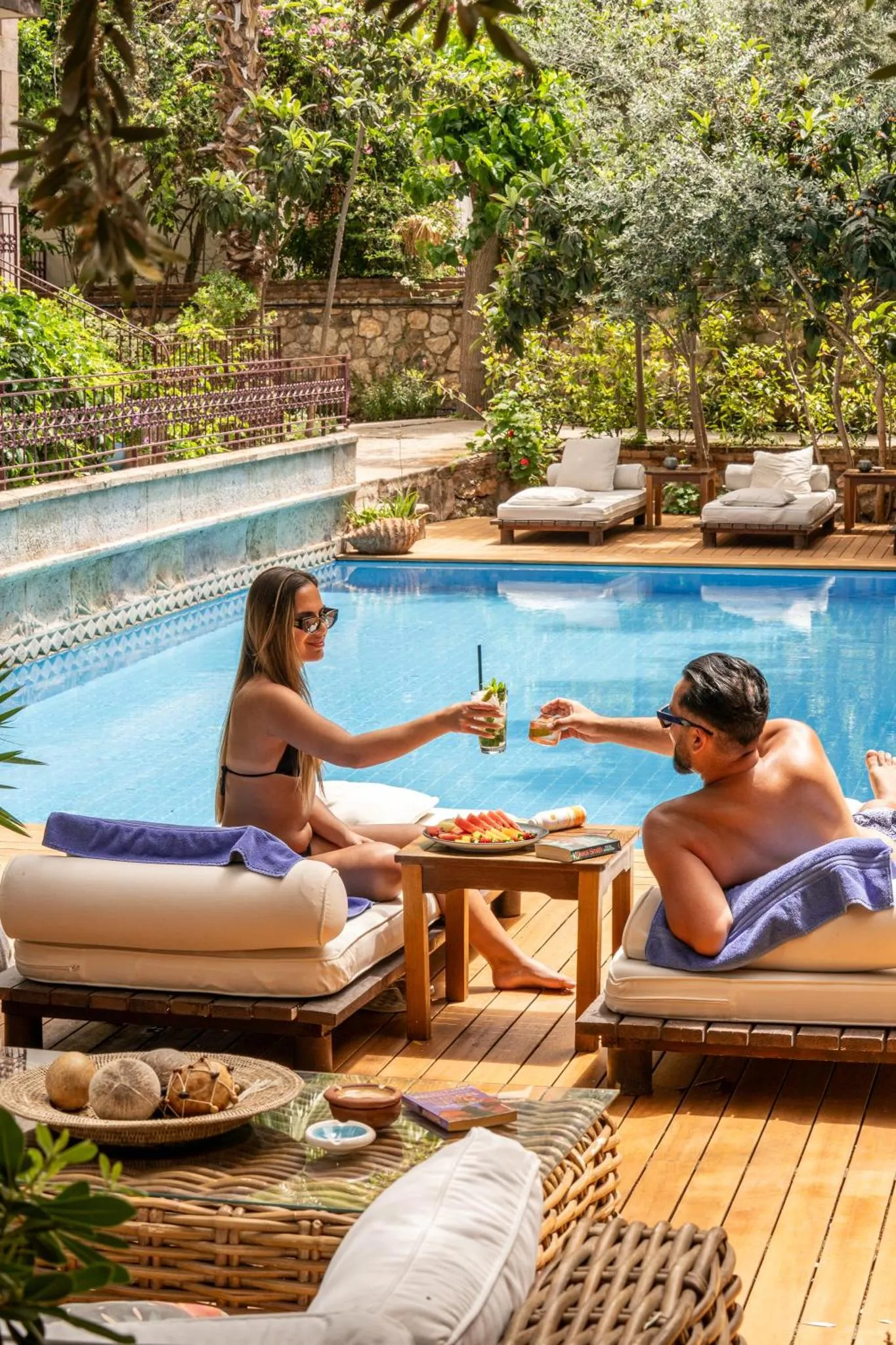 Deux personnes savourent des boissons et des fruits au bord d'une piscine ensoleillée.