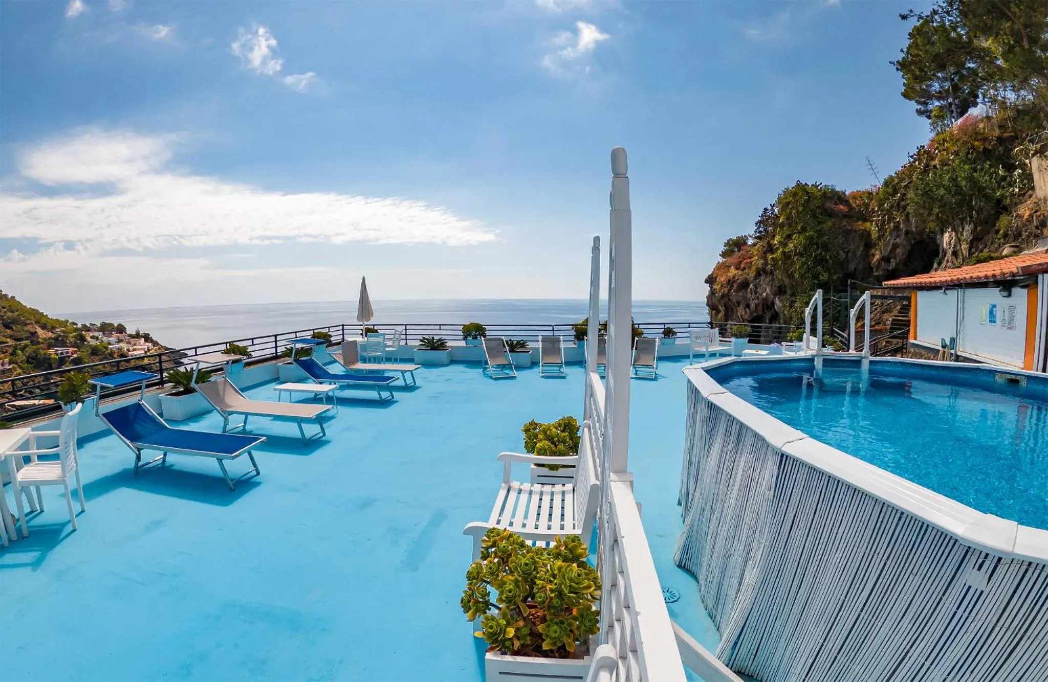 Terrasse avec transats bleus et piscine à débordement offrant une vue sur la mer.
