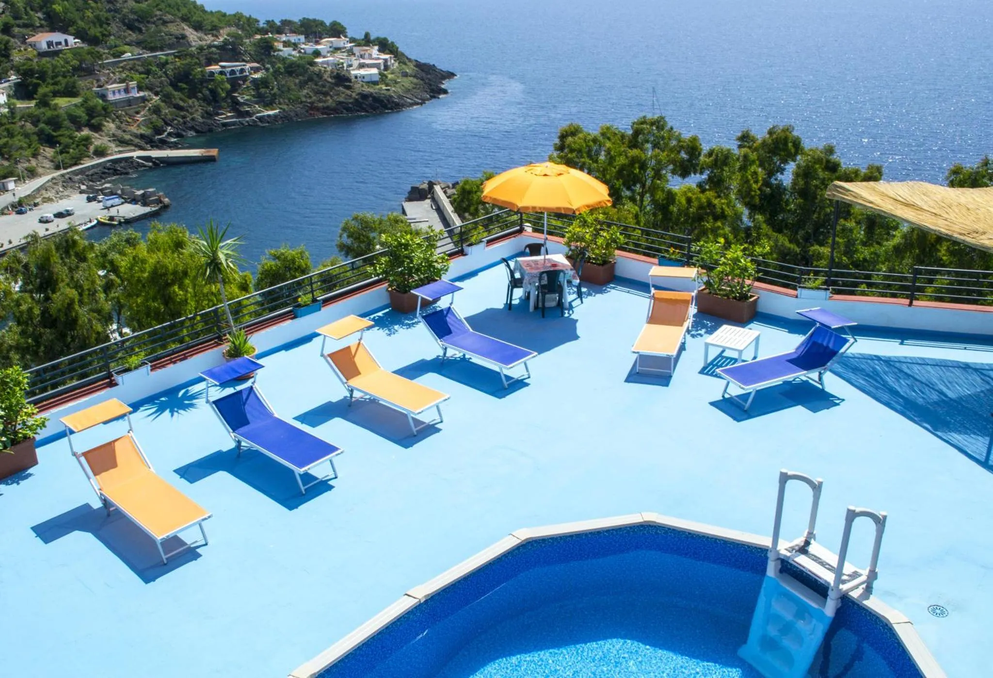 Terrasse avec transats bleus et orange près d'une piscine et vue sur la mer.