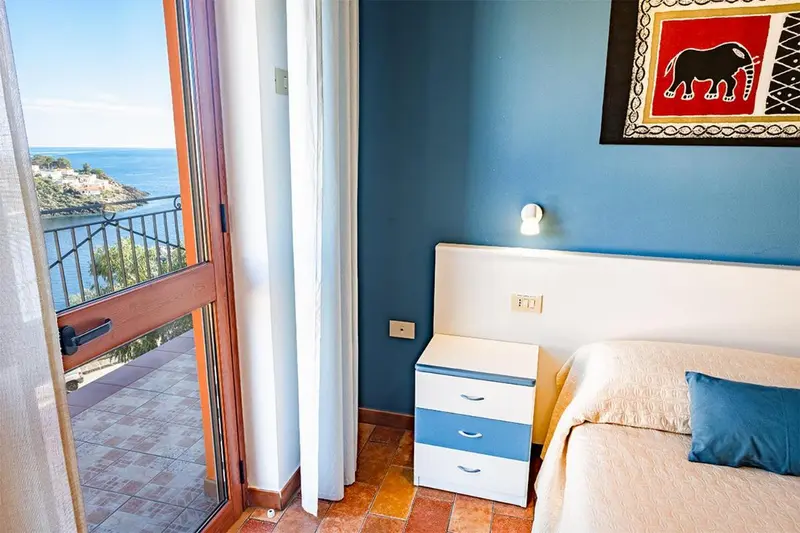 Une chambre lumineuse s'ouvre sur une vue mer par une porte-fenêtre.