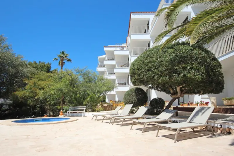 Transats alignés devant un bâtiment blanc avec des balcons et une petite piscine.