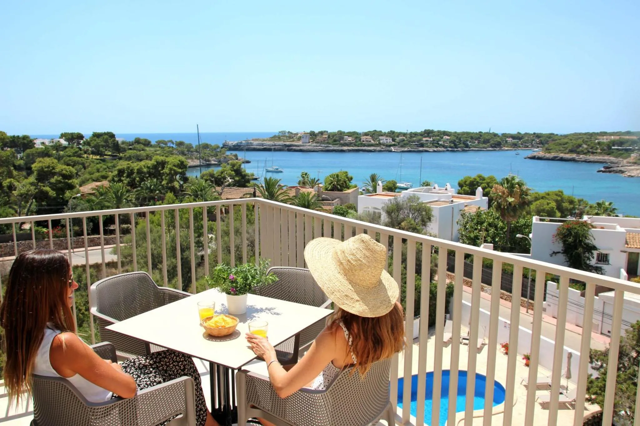 Deux femmes sont assises à une table sur une terrasse ensoleillée avec vue sur la mer.