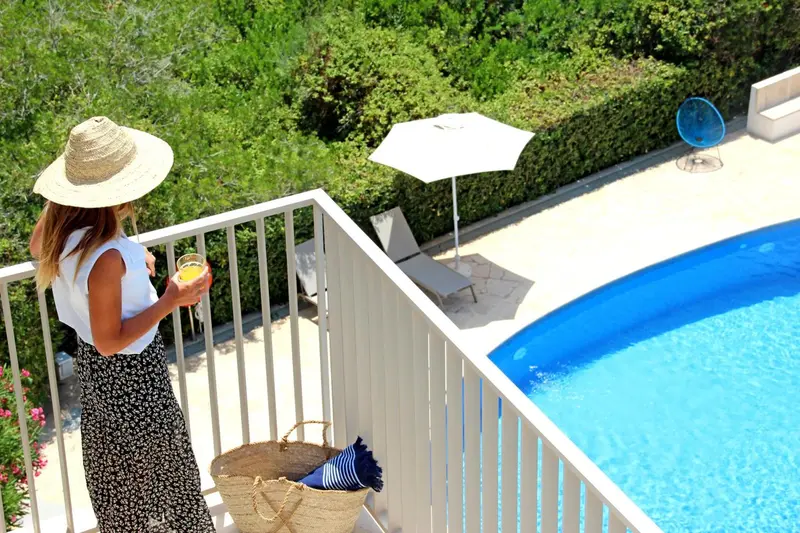 Une personne admire la vue depuis un balcon sur une piscine ensoleillée.