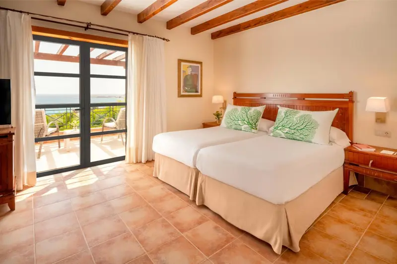 Chambre lumineuse avec un lit double et une vue sur la mer depuis un balcon.