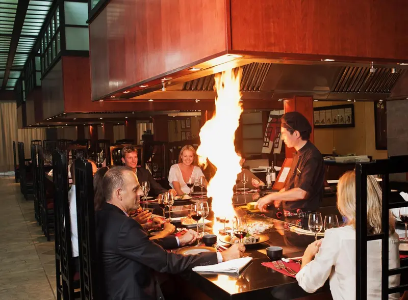 Des clients sont servis dans un restaurant avec un chef cuisinier préparant des plats sur une plaque chauffante.