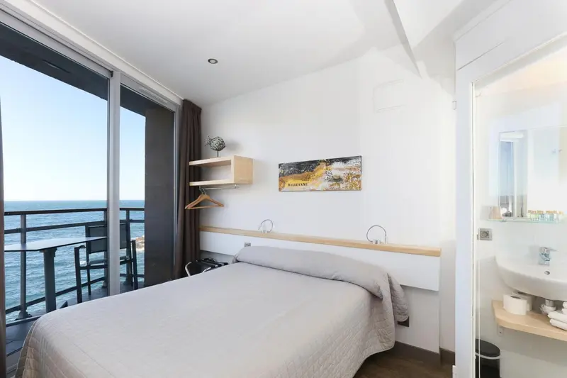 Chambre lumineuse avec un lit simple donnant sur une vue mer.