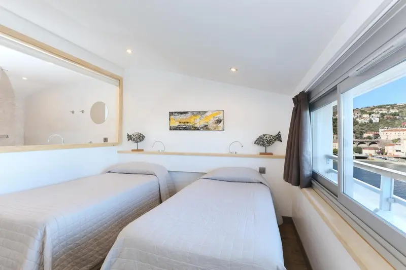 Chambre lumineuse avec deux lits simples et vue sur le port.