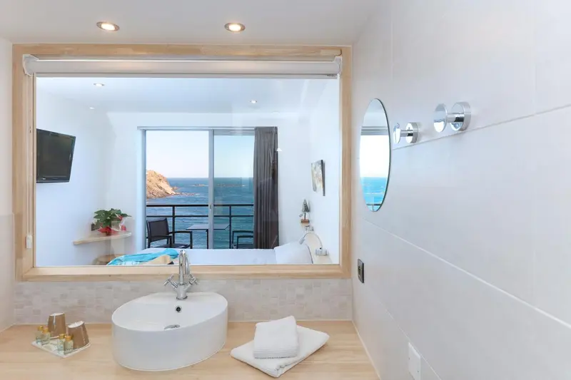 Une salle de bain lumineuse avec un grand miroir et vue sur la mer.