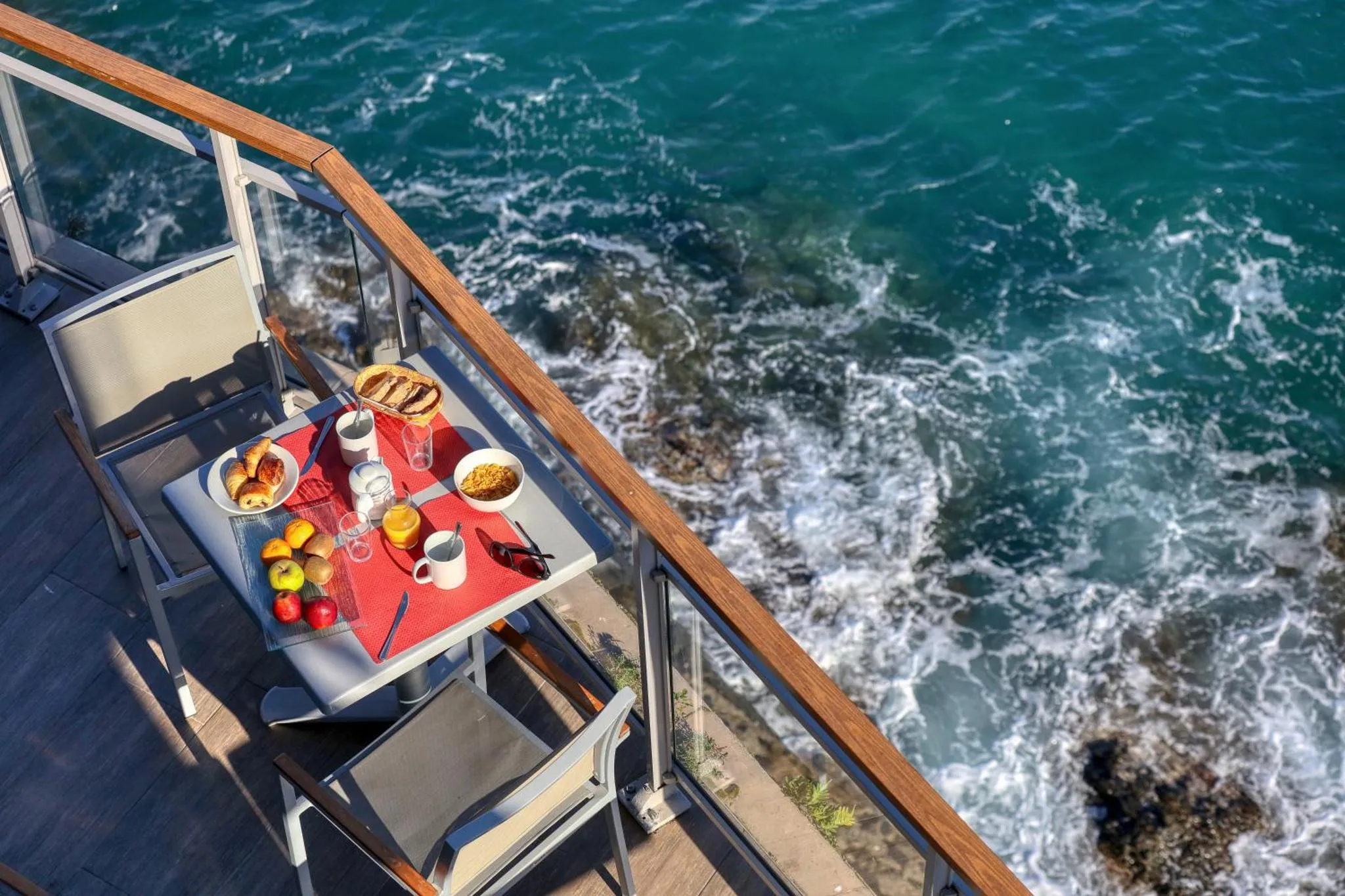 Une table de petit-déjeuner est dressée sur une terrasse en bois avec vue sur la mer.