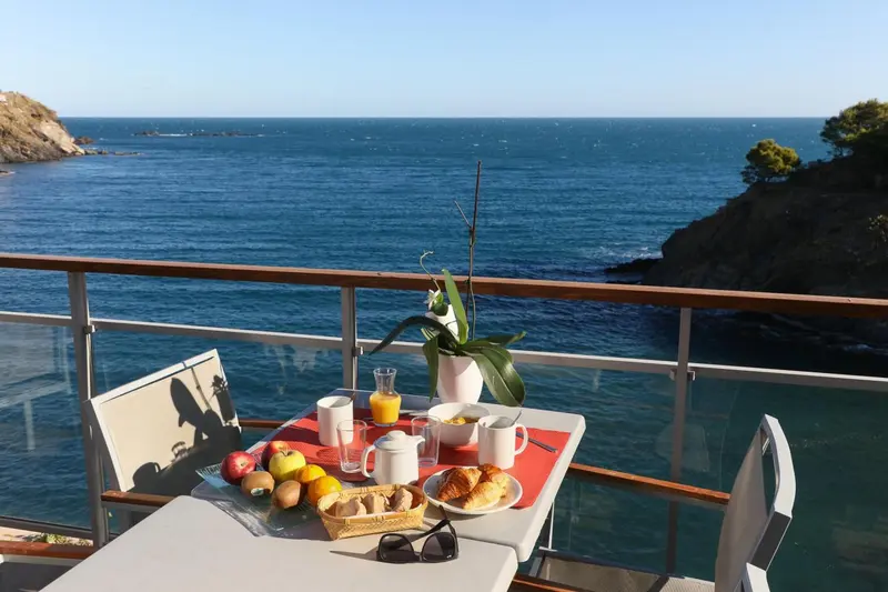Une table de petit-déjeuner est dressée sur une terrasse avec vue sur la mer.