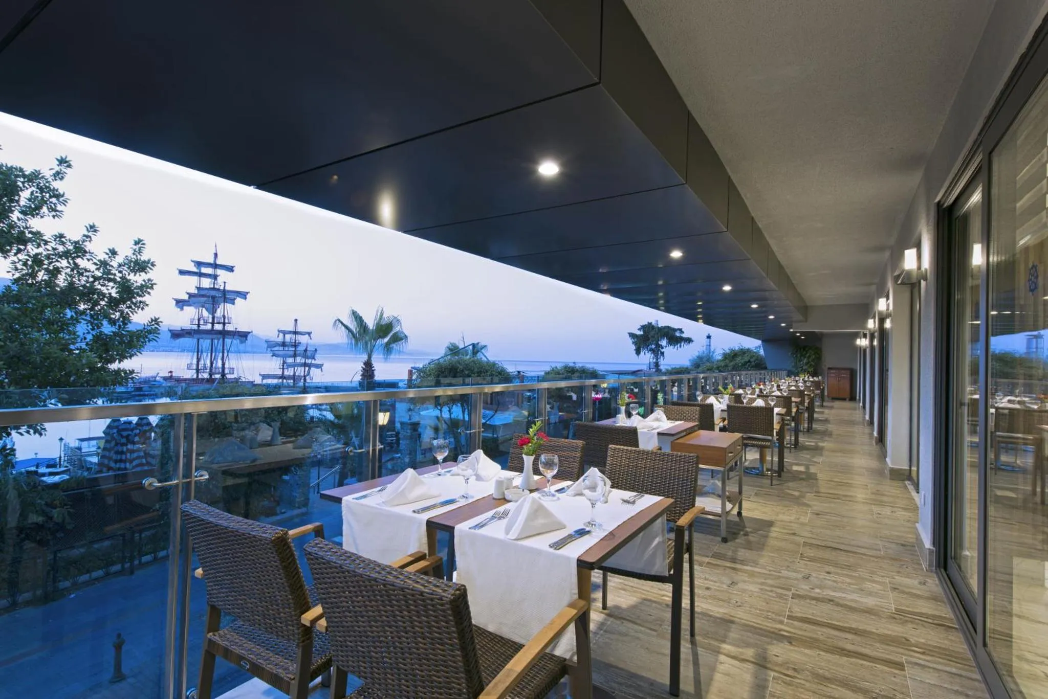 Tables dressées sur une terrasse avec vue sur la mer et un bateau.