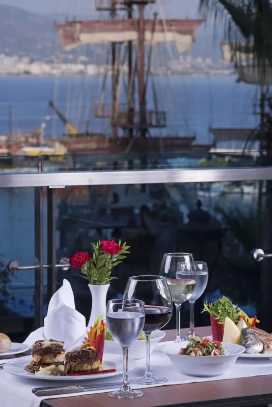 Une table est dressée avec des plats et des boissons, face à un port de plaisance.