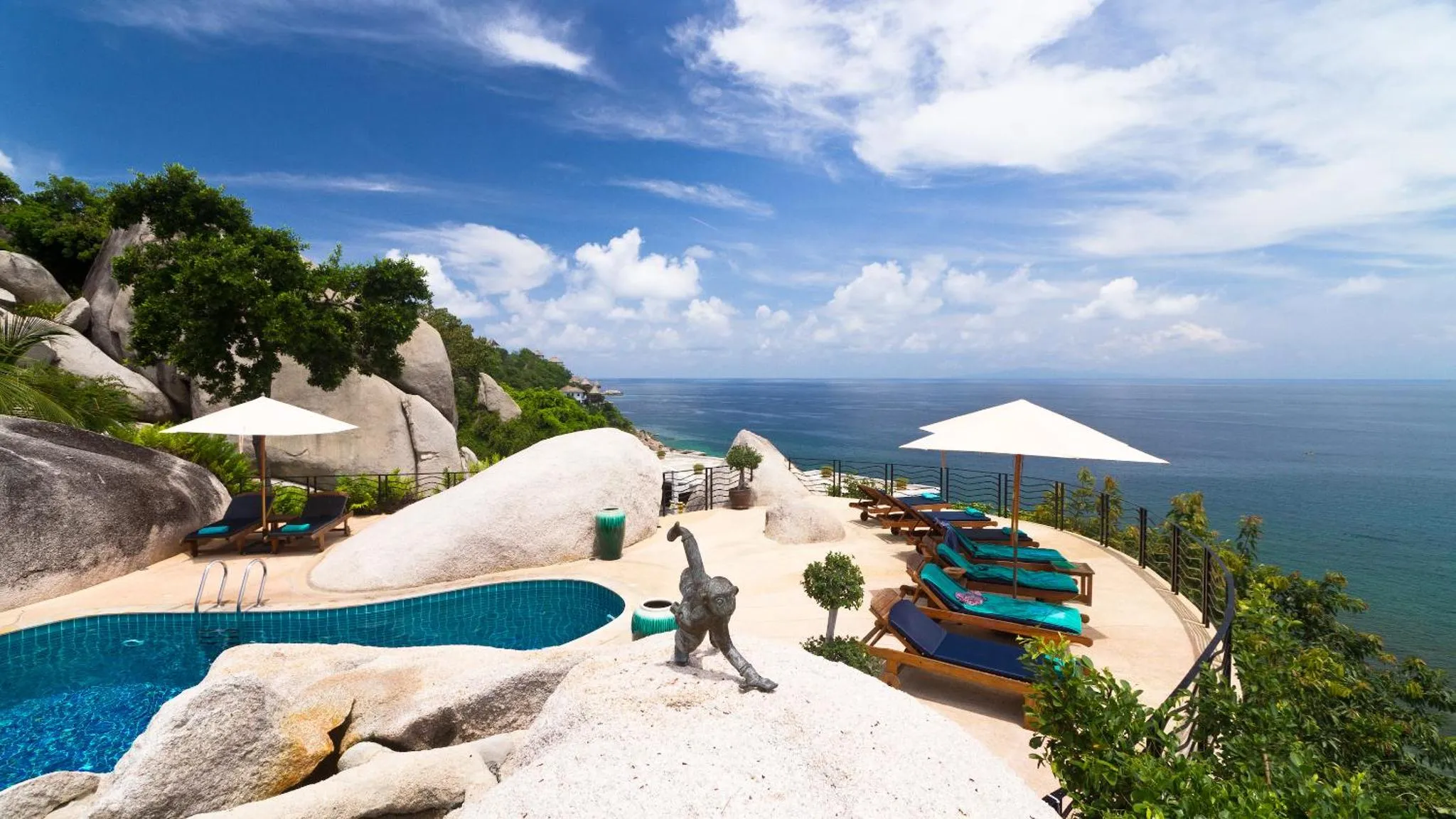 Piscine à débordement avec transats et parasols, surplombant la mer et les rochers.