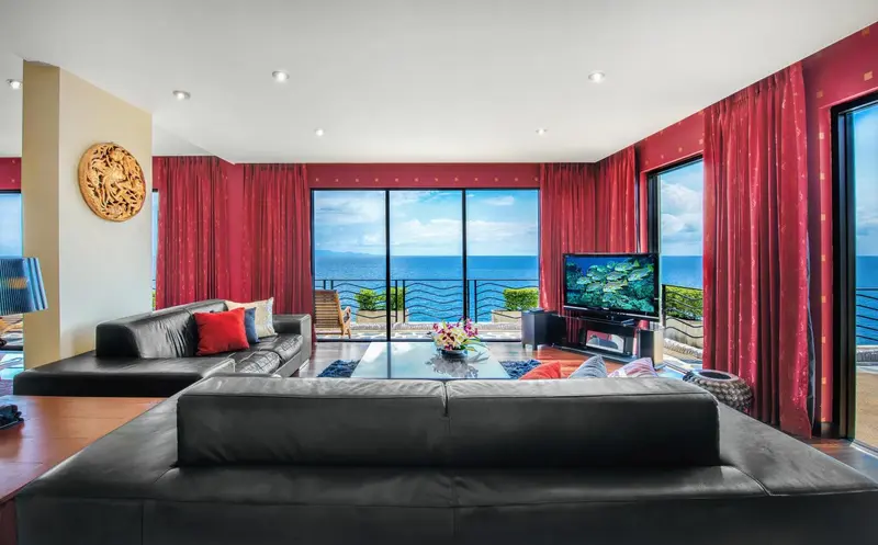 Un salon moderne avec canapés noirs et rideaux rouges offre une vue sur la mer.