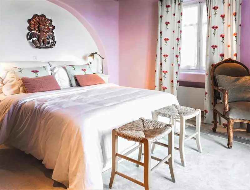 Une chambre lumineuse avec un lit recouvert de linge blanc et des meubles en bois.