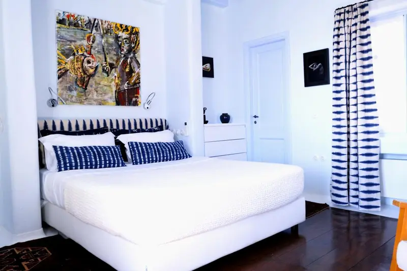 Une chambre lumineuse avec un grand lit recouvert de linge blanc et des coussins bleus.