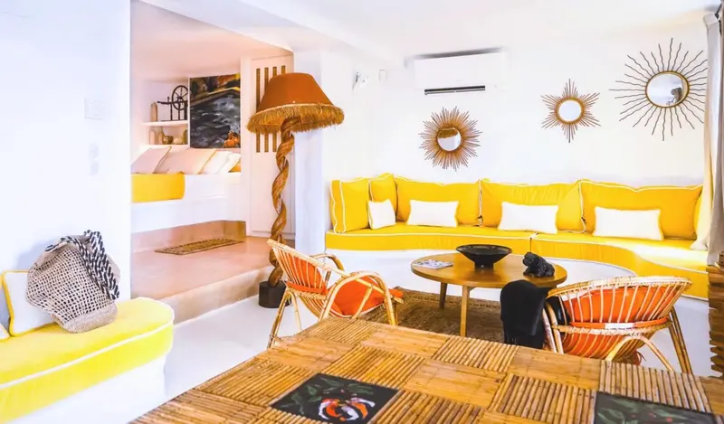 Un salon lumineux avec des canapés jaunes et des fauteuils en rotin.