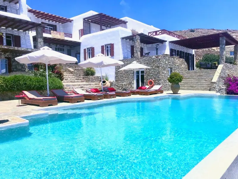Une piscine turquoise bordée de transats et de parasols devant un bâtiment blanc.
