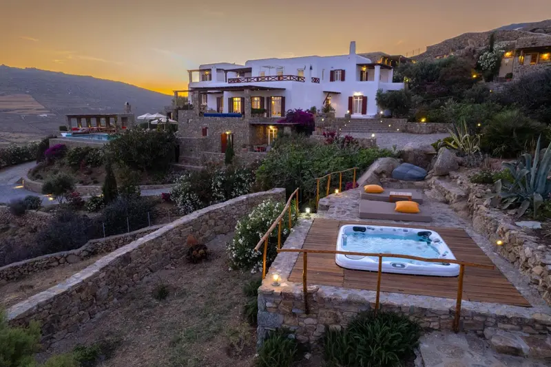 Vue d'un bâtiment blanc illuminé sur une colline, avec un jacuzzi en contrebas.