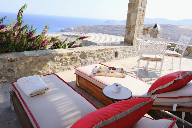 Deux transats avec coussins rouges et une table basse avec des fruits sont disposés sur une terrasse en pierre.
