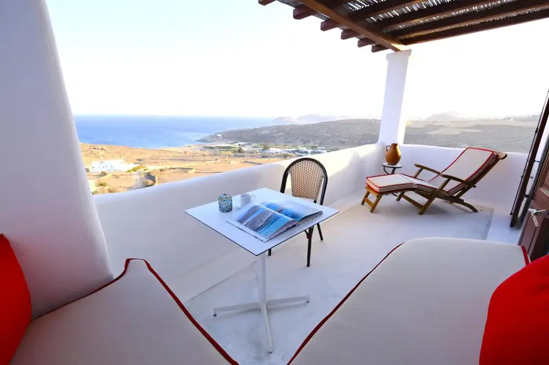 Terrasse blanche avec table, chaises longues et vue sur la mer.