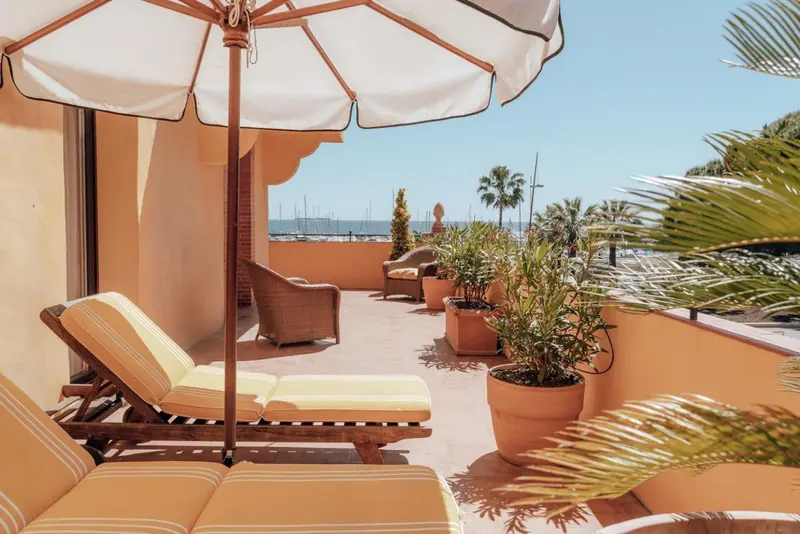 Transats et parasol sur une terrasse ensoleillée avec vue sur la mer.