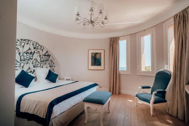 Chambre lumineuse avec un grand lit et un fauteuil bleu.