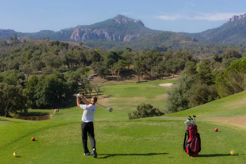 Un golfeur s'apprête à frapper une balle sur un terrain verdoyant avec une vue sur les montagnes.