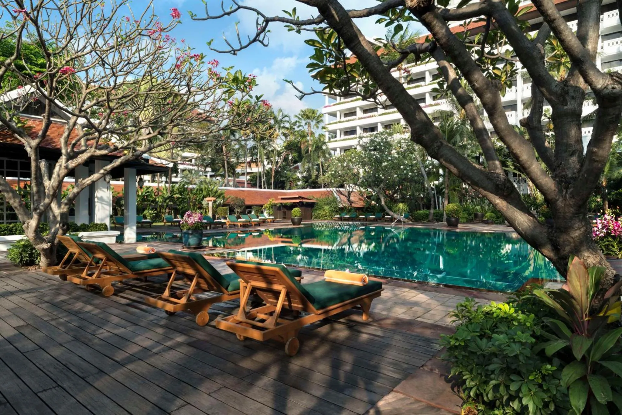 Transats en bois alignés au bord d'une piscine turquoise dans un jardin tropical.