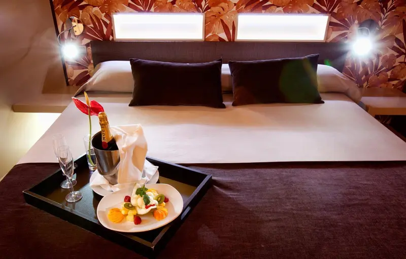 Lit double préparé avec soin dans une chambre d'hôtel, une bouteille et des fruits frais sur une table basse.
