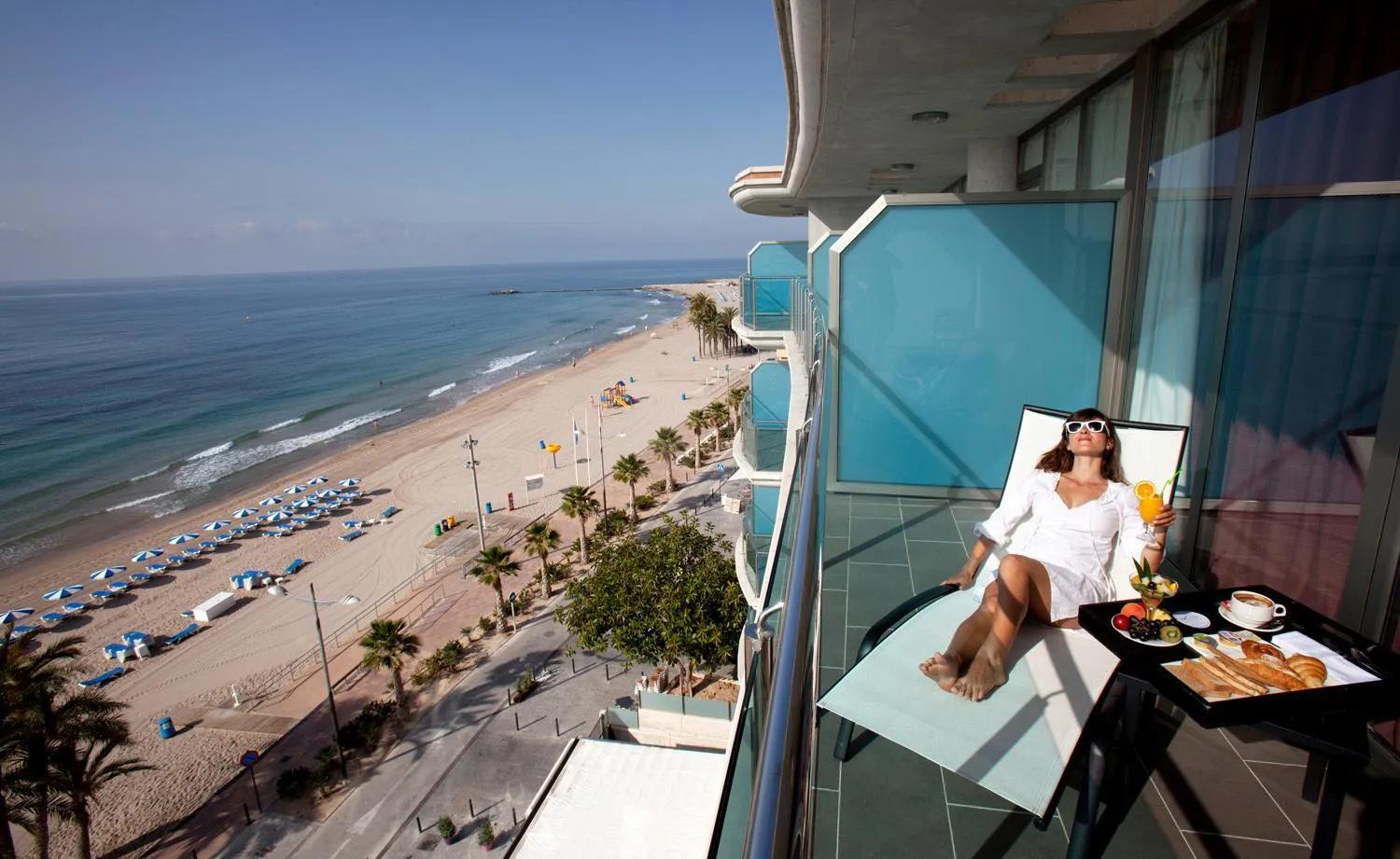 Une personne se détend sur un balcon avec une vue sur la mer et la plage.