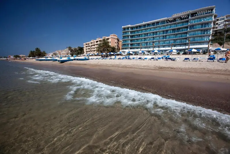 Vague déferlant sur une plage de sable fin devant un bâtiment hôtelier.