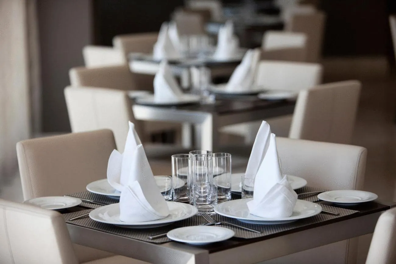 Une table est dressée dans une salle de restaurant avec des couverts et des serviettes en tissu.