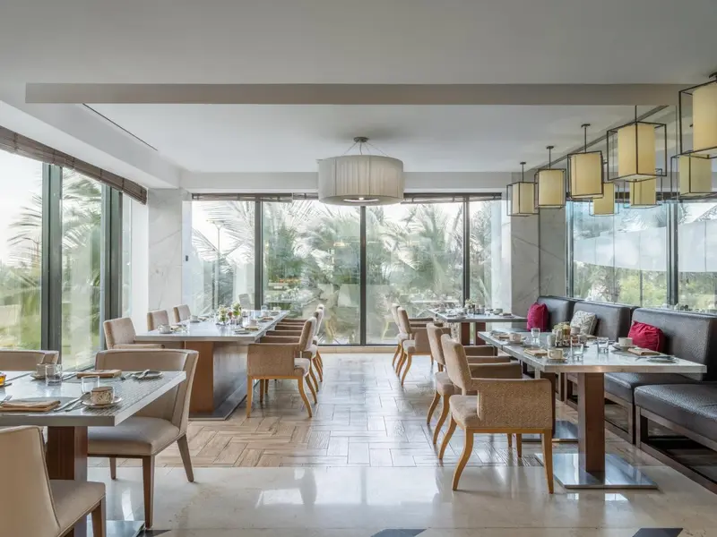 Une salle lumineuse avec des tables dressées près de grandes baies vitrées.