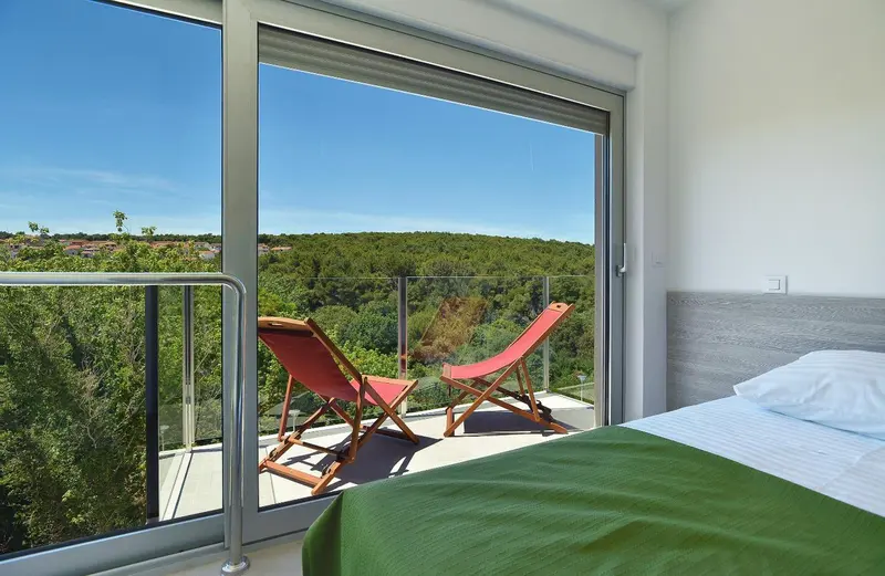 Une chambre lumineuse s'ouvre sur une terrasse avec vue sur la végétation.