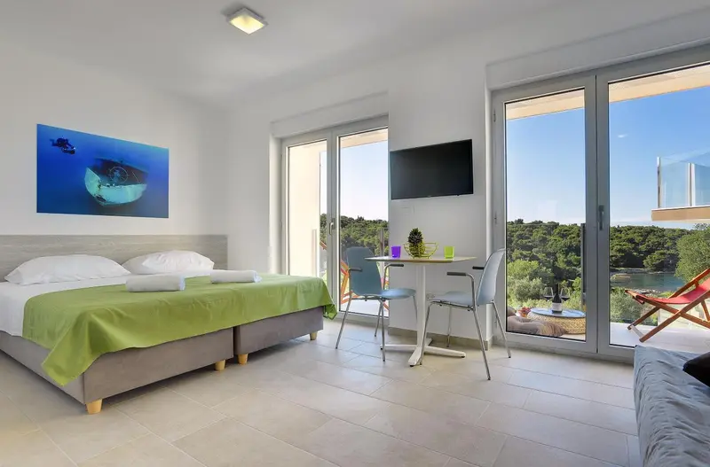 Une chambre lumineuse avec un grand lit et un coin repas près d'une baie vitrée.