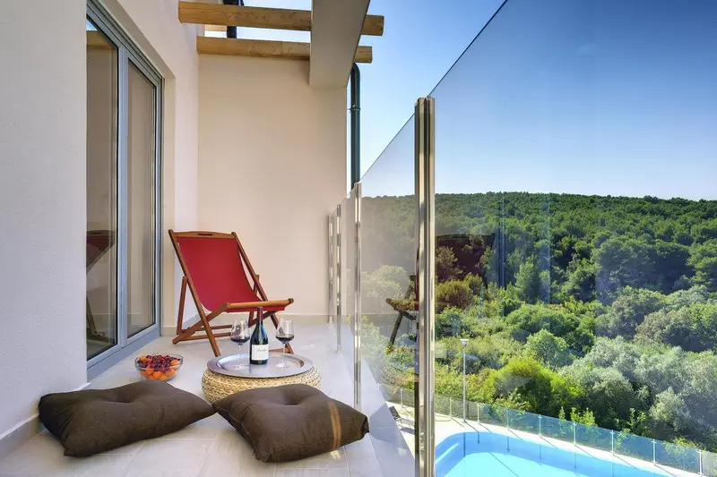 Une terrasse avec un fauteuil rouge, une table basse et des coussins offre une vue sur la végétation.