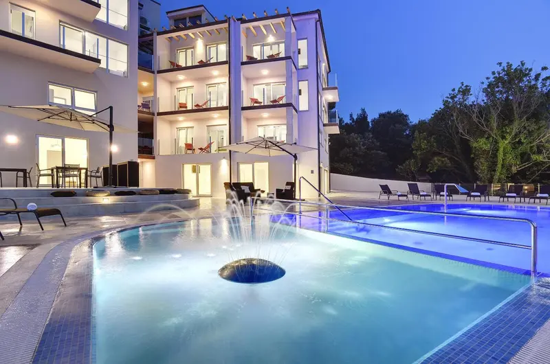 Une piscine illuminée avec une fontaine et des transats.