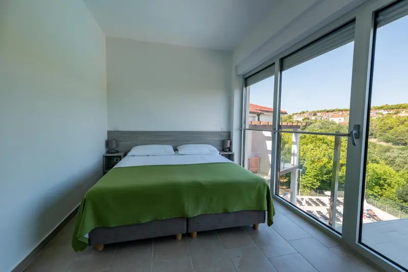 Une chambre lumineuse avec un grand lit et une vue sur la végétation.